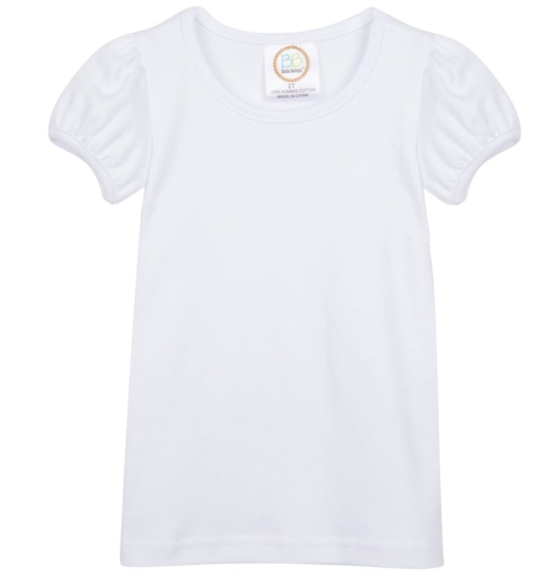 May include: White short-sleeved t-shirt with a round neckline and puffed sleeves. The shirt has a small tag with the text "Baby Boutique 2T 100% Combed Cotton Made in China" on the front.
