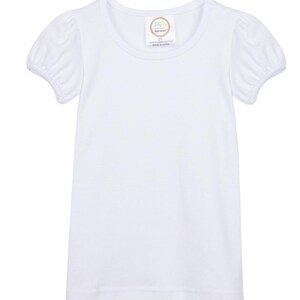 Peut inclure: T-shirt blanche &agrave; manches courtes avec un col rond et des manches bouffantes. Le t-shirt a une petite &eacute;tiquette avec le texte "Baby Bows" et "100% coton peign&eacute; fabriqu&eacute; en Chine".