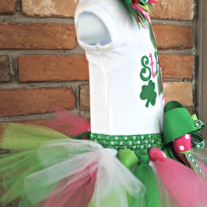 Peut inclure: Un body blanc avec un tr&egrave;fle vert et le texte "St. Patty's Day" en rose et vert. Le body est associ&eacute; &agrave; un tutu en tulle vert, rose et blanc avec un n&oelig;ud vert et rose.