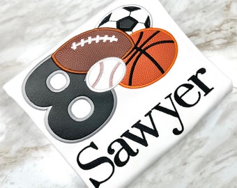 May include: A white t-shirt with a black number eight, a baseball, football, basketball, and the name Sawyer embroidered on it.