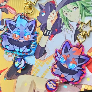 Puede incluir: Dos llaveros acrílicos con personajes de dibujos animados con detalles en azul, morado y naranja. Cada llavero tiene un cierre dorado en forma de estrella y un pequeño dije. Los llaveros se exhiben sobre un fondo colorido con otros personajes de dibujos animados.