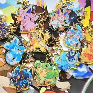 May include: A selection of colourful acrylic keychains featuring cartoon characters. Each keychain has a gold star charm and a gold chain. The characters are in various poses and colours.