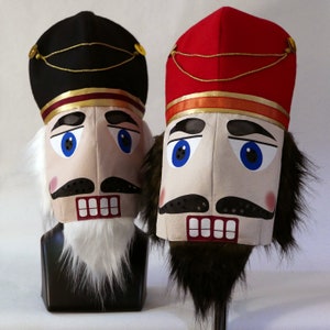 May include: Two nutcracker head masks, one with a black hat and white beard, the other with a red hat and brown beard.
