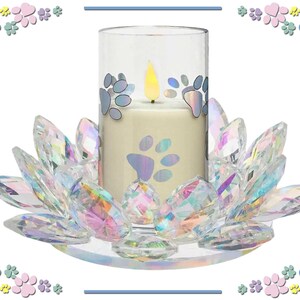 May include: A decorative candle holder featuring a cream-colored candle with paw print decals inside a clear glass cylinder. The candle sits on a clear, iridescent crystal lotus flower base. The candle has a faux flame.
