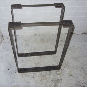 May include: Two black metal table legs, stacked on top of each other. The legs are square and have a simple design.