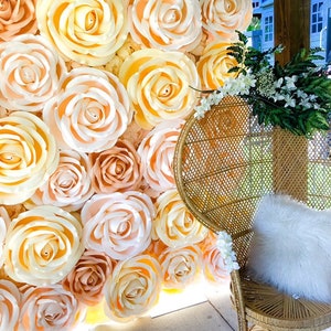 May include: A wall decorated with large, paper, peach and cream colored roses. A wicker chair with a white faux fur cushion sits in front of the wall.