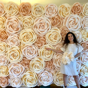 May include: A large wall backdrop made of paper flowers in shades of cream and peach. The flowers are arranged in a repeating pattern and create a romantic and elegant look.