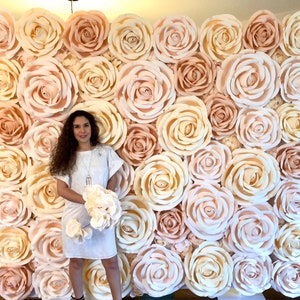 May include: A large wall of paper flowers in shades of cream and blush. The flowers are arranged in a grid pattern and create a beautiful backdrop for a photo shoot or event.