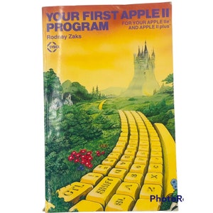 May include: A vintage book cover with a yellow background and the title "Your First Apple II Program" by Rodney Zaks. The cover features a yellow brick road leading to a castle in the distance, with a keyboard made of yellow bricks.