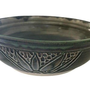 Może przedstawiać: Zielona ceramiczna miska z dekoracyjnym wzorem kwiatowym. Miska ma szeroki rant i zaokrąglone dno.