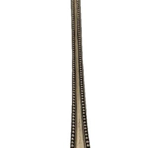 May include: A long, slender silver-toned metal cocktail fork featuring three tines and a decorative handle. The handle is adorned with a beaded border along the edges and an ornate, scrolled pattern at the base, showcasing a metallic finish.