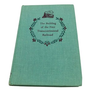 May include: A teal green book with a maroon and green illustration of a train and a wreath of flowers. The text on the cover reads "The Building of the First Transcontinental Railroad".