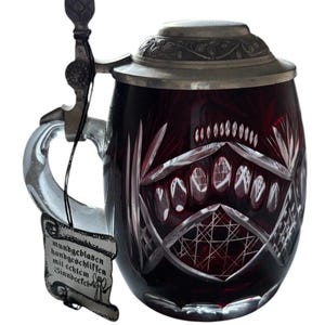 May include: A red glass beer stein with a silver lid and handle. The stein is decorated with a cut glass design and the text "mundgeblasen handgeschliffen mit echtem Zinn-Deckel".