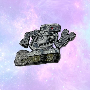 Puede incluir: Un robot plateado con ojos rojos y un brazo de llave inglesa. El robot está sobre una base tipo tanque con una estela de humo gris y negro detrás.