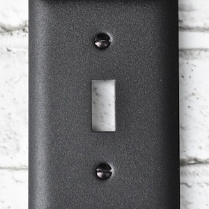 May include: Black single-gang electrical wall plate with a single toggle switch opening. The plate has a textured finish.