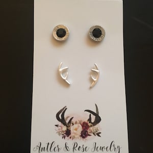 May include: A white card displays two pairs of earrings. One pair features black gemstone studs set in silver casings. The other pair is silver antler-shaped earrings. The card has a floral antler design and reads "Antler & Rose Jewelry."
