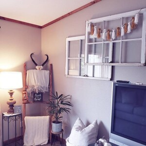 May include: A cozy interior scene with Halloween decorations. A white window frame is adorned with a ghost garland. A wooden ladder displays a skull, blanket, and a sign that reads "trick or treat". A lamp and a plant add to the decor.