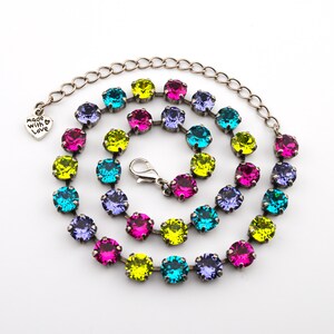 May include: A silver-toned necklace with a series of colorful, round gemstones in shades of teal, purple, pink, and yellow. The necklace has a lobster clasp closure and a heart-shaped charm that reads "made with love."