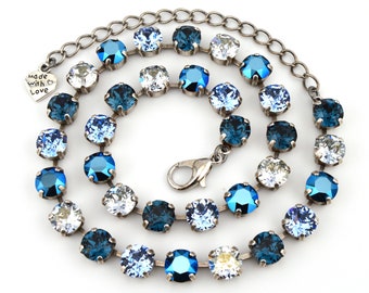 May include: A necklace featuring a series of round, faceted crystals in shades of blue, light blue, and clear, set in a silver-toned metal chain. The necklace includes a lobster claw clasp and a small heart-shaped charm engraved with Made with Love.