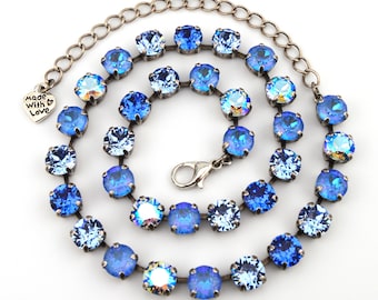 May include: A necklace featuring a series of round, faceted blue crystals set in dark metal prongs. The chain includes a lobster claw clasp and a small heart-shaped charm engraved with the text Made with Love at the end of the extender chain.