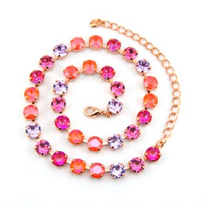 May include: A rose gold tone necklace featuring a series of round, faceted crystals in alternating shades of bright orange, hot pink, and light purple. The chain includes a lobster claw clasp and an adjustable extender link section at the end.
