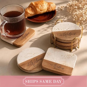 May include: A set of round and square coasters made of light-colored stone and wood, featuring the engraved text The Wilsons Est 2025. The coasters are displayed with a ribbed glass mug filled with dark liquid and a croissant on a small plate.