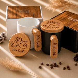 May include: A white ceramic mug and a black ceramic mug, each featuring a wooden handle and a matching wooden lid. The lids are engraved with 50 years love and a heart symbol, while the handles are engraved with Mrs. Smith and Mr. Smith.