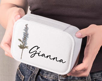 May include: A white rectangular travel jewelry case featuring a printed illustration of a blue delphinium flower and the name Gianna written in black cursive script. The case has a textured fabric exterior and rounded corners on the lid.