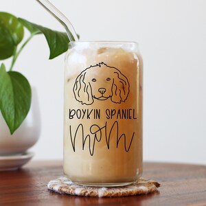 May include: A clear glass can with a straw, filled with a light brown beverage. The can has a black and white illustration of a Boykin Spaniel dog and the text "Boykin Spaniel Mom".