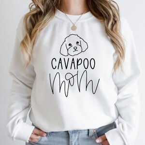 Könnte beinhalten: Weißer Pullover mit einer schwarzen Umrandung eines Cavapoo-Hundes und dem Text "Cavapoo Mom" in schwarzer Schrift.