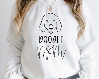 May include: White sweatshirt with a black doodle dog graphic and the text "DOODLE MOM". The design is minimalist and stylish, suitable for casual wear. The sweatshirt is a comfortable, relaxed fit.