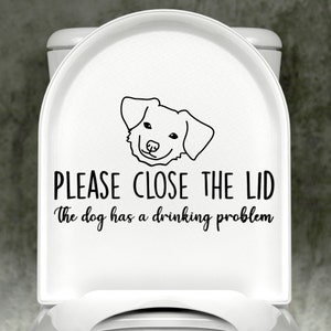 May include: White toilet seat with a black and white sticker that says "Please close the lid. The dog has a drinking problem." and a cartoon dog illustration.