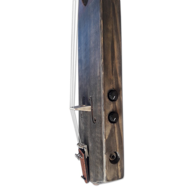 May include: A wooden electric violin with a dark gray stain. The violin has a brown leather strap and two black knobs on the side.