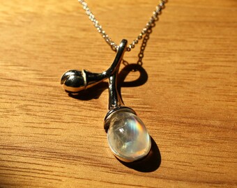 May include: A silver necklace with a delicate branch pendant featuring a pearlescent moonstone. The pendant has a small bud at the top and a larger moonstone at the bottom.