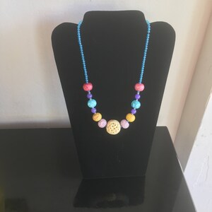May include: A colorful beaded necklace with a light blue string and a variety of colored beads, including pink, yellow, turquoise, and red.