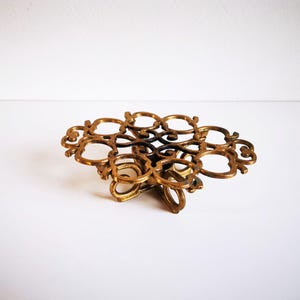 Può includere: Vassoio decorativo in ottone in stile vintage. Presenta un complesso design traforato con molteplici elementi circolari e curvi. L'ottone ha una calda patina invecchiata, che suggerisce la sua origine. Probabilmente utilizzato per scopi decorativi.