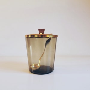 Può includere: Un distributore di zucchero in vetro con un coperchio dorato e un pomello in legno. Il distributore contiene un mestolo dorato abbinato.