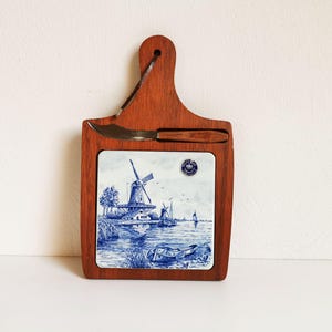 May include: Wooden cheese board with a blue and white Delftware tile featuring a windmill scene. Includes a small cheese knife. The board is approximately 10 inches long.
