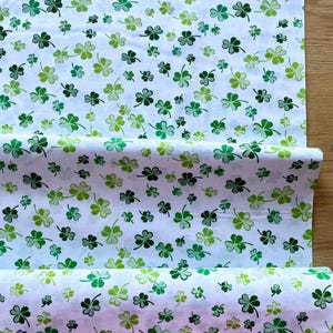 May include: White fabric with a repeating pattern of green shamrocks in various shades. The fabric is folded and rolled, showcasing the clover design. Ideal for St. Patrick's Day crafts or decor.