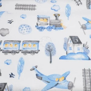 Op de afbeelding: Een witte stof met een herhalend patroon in blauw en grijs van treinen, vliegtuigen, huizen en bomen. Het patroon is een fantasierijk ontwerp voor kinderbeddengoed of stof.
