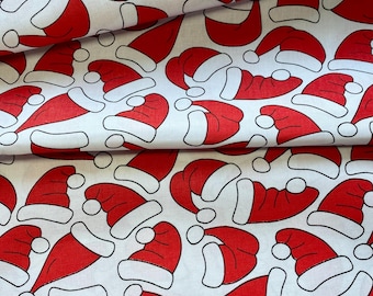 May include: White fabric with a repeating pattern of red Santa hats. Each hat has a white brim and a white pom-pom. The hats are in various orientations, creating a festive and playful design, perfect for holiday-themed crafts.