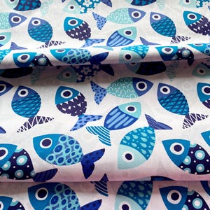 May include: White fabric with a repeating pattern of stylized blue fish. The fish vary in shades of blue and have different patterns, including dots, stripes, and floral designs. The fabric is likely cotton or a similar material.