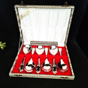 Könnte beinhalten: Ein Set silberfarbener Löffel und Servierutensilien, präsentiert in einer dekorativen Box mit rotem Samtinterieur. Die Box ist geöffnet und zeigt das Besteck vor einem weißen Satinfutter. Auf der Box steht "Grosvenor Plate".
