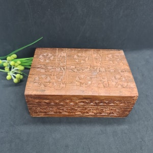 May include: A rectangular wooden box with detailed floral carvings on the lid and sides. The box is a warm brown colour and appears to be made of wood. The carvings are intricate and add a decorative element to the box.