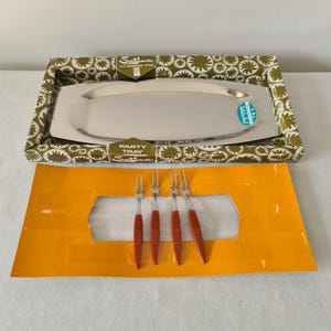 May include: A vintage party tray set with a stainless steel serving tray and four serving forks. The tray is rectangular and sits in a patterned box. The forks have silver tines and red handles.