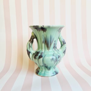 May include: A vintage ceramic vase in shades of mint green and dark brown. The vase has a flared top, two side handles, and a pedestal base. The glaze has a dripped effect, adding to its unique, retro aesthetic.