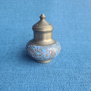 Op de afbeelding: Een kleine, antieke metalen container met een deksel. De container heeft een bolvormige basis met een lichtblauw emaille ontwerp en gouden accenten. Het deksel is van donkerder metaal met een punt.