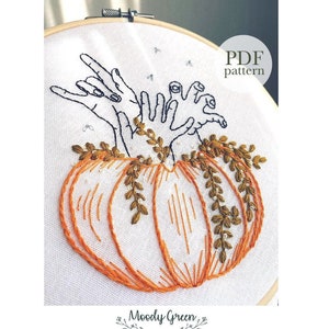 May include: Embroidered design of two hands reaching out of a pumpkin with green vines. The design is in a white embroidery hoop. The text "PDF pattern" is in the upper right corner of the image.