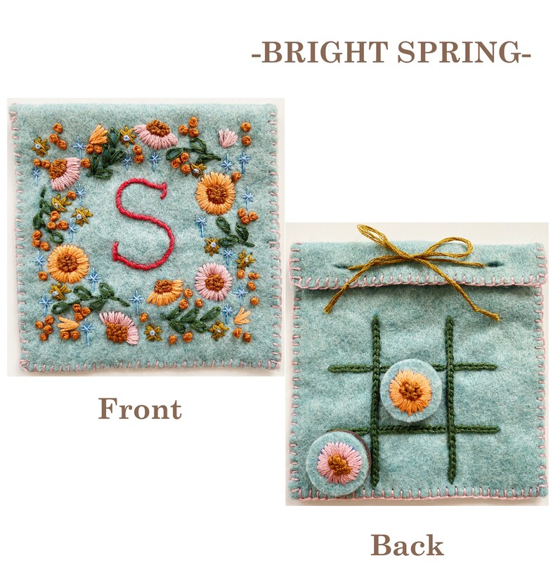 May include: A light blue felt pouch with a floral embroidery design and the letter "S" on the front. The back of the pouch has a noughts and crosses board with two embroidered circles.