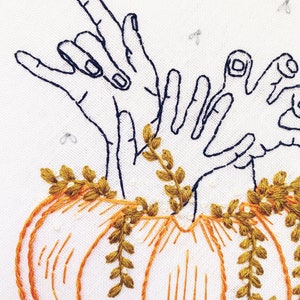 May include: Embroidered design of two hands reaching out of a pumpkin with green vines. The pumpkin is orange and the hands are black.